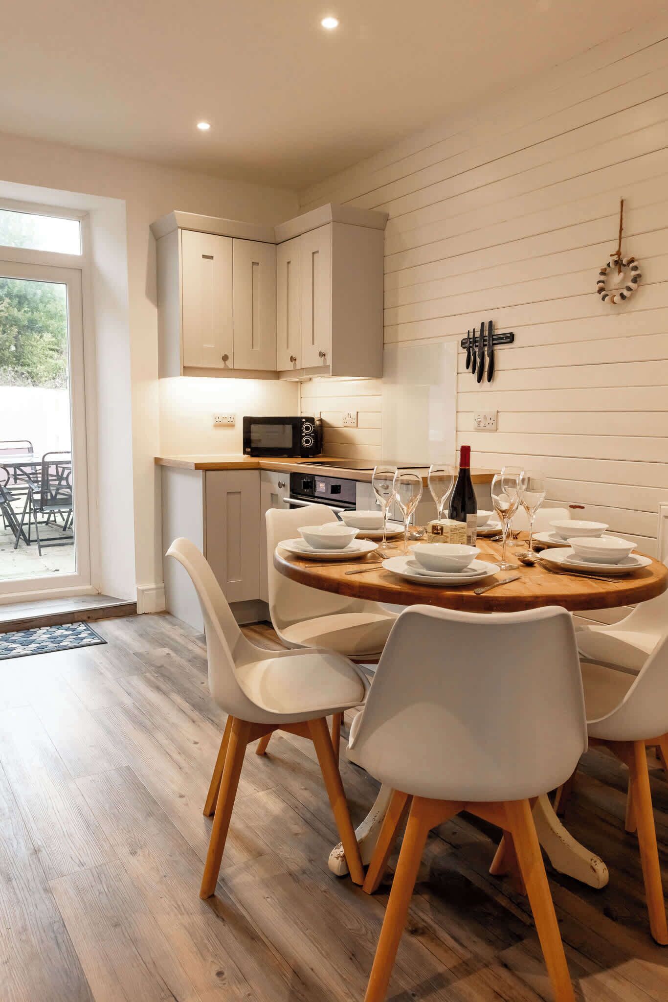 A modern kitchen with white cabinetry, a microwave, and a dining area with a round wooden table set for four.