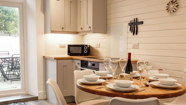 Cozinha moderna com armários brancos, micro-ondas e sala de jantar com mesa redonda de madeira para quatro pessoas.