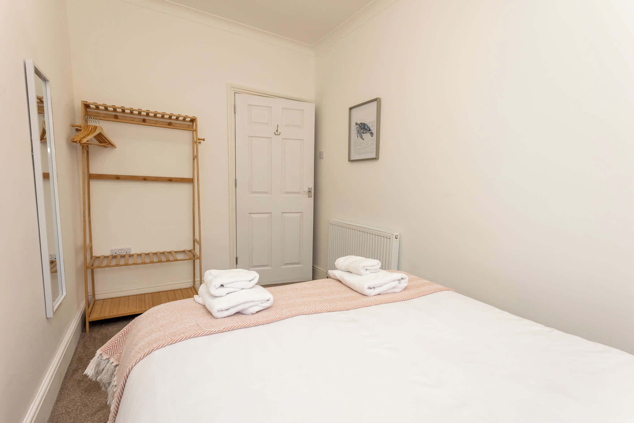 A bedroom with a bed, a wooden wardrobe, a radiator, and a framed picture on the wall.