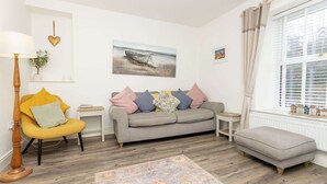 Sala de estar com sofá, poltrona, banquinho e tapete.