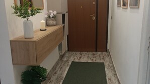 A hallway with a wooden floor, a green mat, a wooden cabinet, a mirror, a potted plant, a door, and framed pictures on the wall. - Valle dei Casali House is 5 minutes from Villa Pamphili and 15 minutes from the Vatican. (Roma)