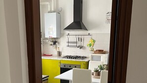 A modern kitchen with a gas stove, white cabinets, a black range hood, hanging light bulbs, and a dining area with a white table and chairs. - Valle dei Casali House is 5 minutes from Villa Pamphili and 15 minutes from the Vatican. (Roma)