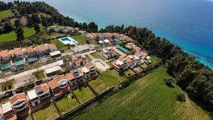 Vista aérea de una zona residencial costera con casas, una piscina y una vista despejada del mar.