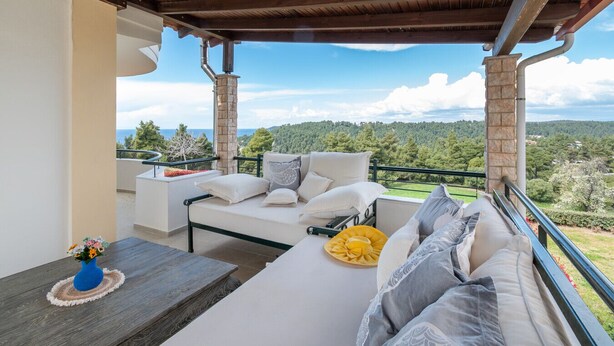 Un balcón con sofá y mesa, vista al paisaje y un pilar de piedra.