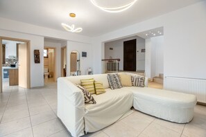 A modern living room with a sectional sofa, a dining area, and a staircase leading to another floor.