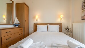 Una cama bien hecha con sábanas blancas, un aparador de madera con cajones y dos lámparas de pared.