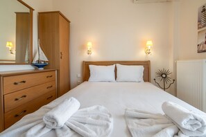 Un lit bien fait, avec du linge de lit blanc, une commode en bois dotée de tiroirs et deux lampes fixées au mur.