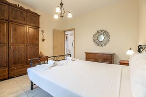A bedroom with a large bed, wooden wardrobe, a mirror, and a chandelier.