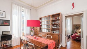 Un comedor con una mesa de madera, sillas, una lámpara roja y un aparador de vidrio con vajilla.