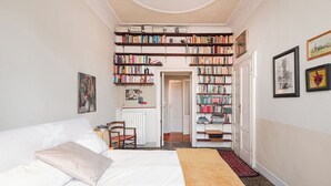 Un dormitorio con cama, una silla, una estantería y un radiador.