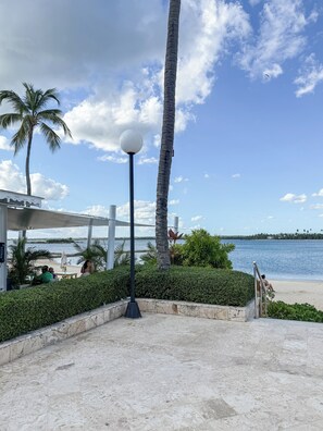 A beachside area with a covered seating area, a palm tree, and a lamp post. - Vista Gold II Bahia Principe (Ramon Santana)