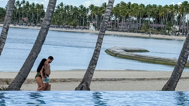 Poolbereich mit Palmen, Strand und blauem Himmel.