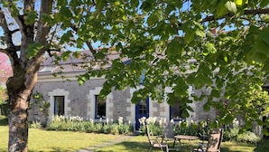Ein Steingebäude mit Garten, Sitzgelegenheiten im Freien und einem Baum im Vordergrund.