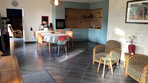 Ein Essbereich mit Tisch und Stühlen, eine Küche mit blauen Schränken und ein Wohnzimmer mit gemusterten Sesseln.
