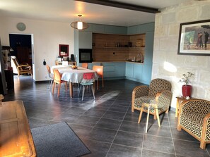 A dining area with a table and chairs, a kitchen with blue cabinets, and a living room with patterned chairs.