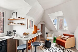 A modern loft with a kitchen, dining area, and a cozy seating area with a red chair and a small table. - Chic 1BR Near Golden Triangle & Eiffel Tower (Paris)