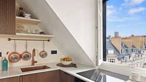 Eine Küche mit einem großen Fenster, Kupferkochgeschirr, einer Obstschale und Blick auf Gebäude.