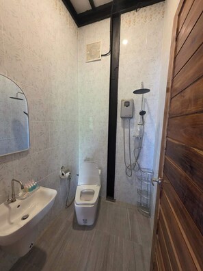 A bathroom with a toilet, sink, shower, and wooden paneling.