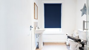 Ein Badezimmer mit einem weißen Waschbecken, einer Toilette und einem Fenster mit blauer Jalousie.