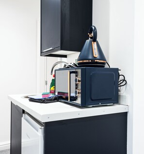 Una cucina compatta con forno a microonde, bollitore e un piccolo mobiletto.