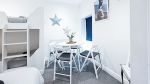 Ein Zimmer mit einem Etagenbett, einem runden Tisch mit Stühlen, einer Topfpflanze und einem gerahmten Bild an der Wand.