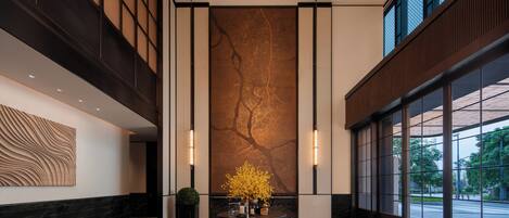 A lobby with a central round table, a large wall mural, and large windows.