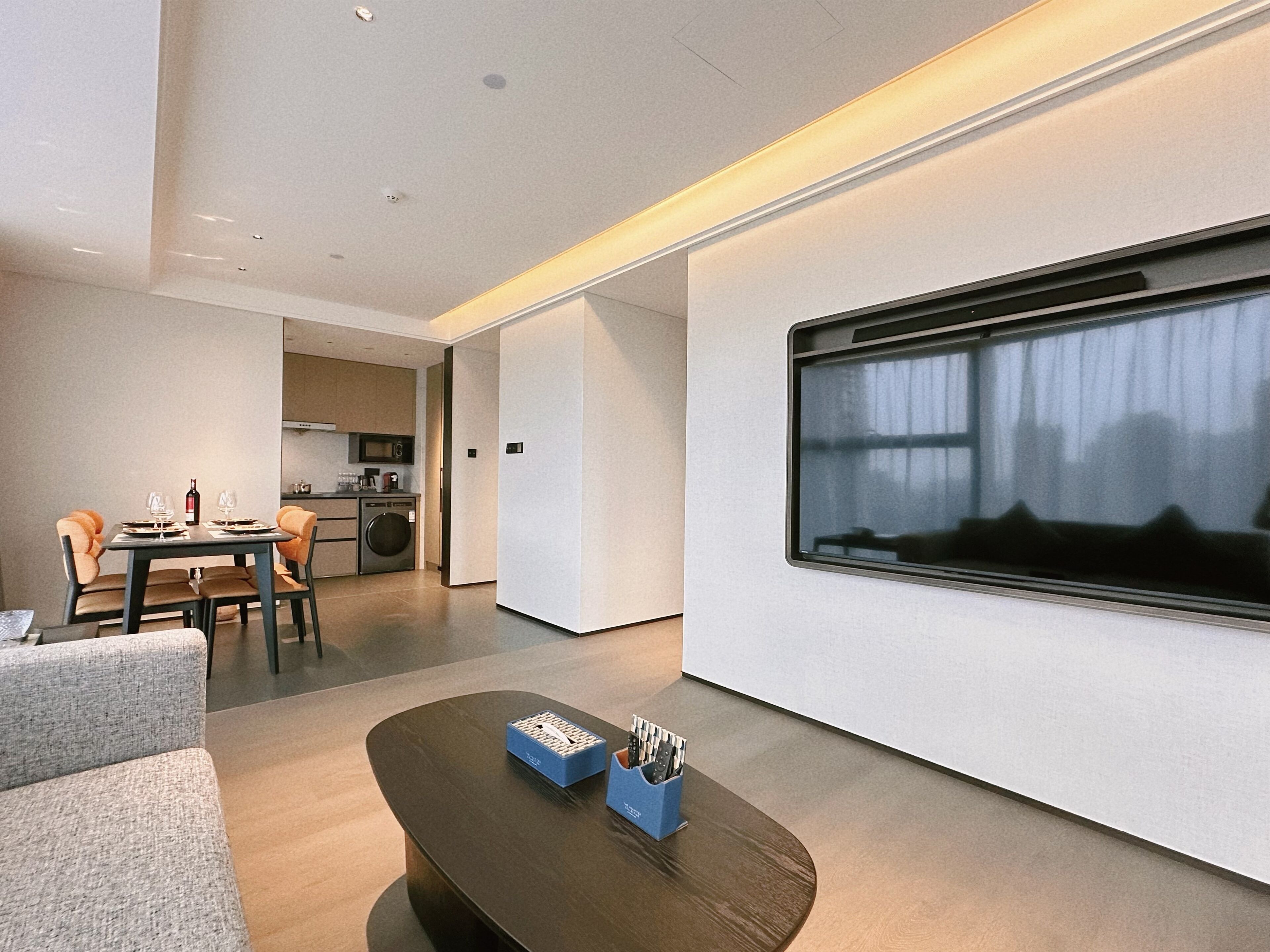 A modern living room with a dining area, a kitchen, and a large window.