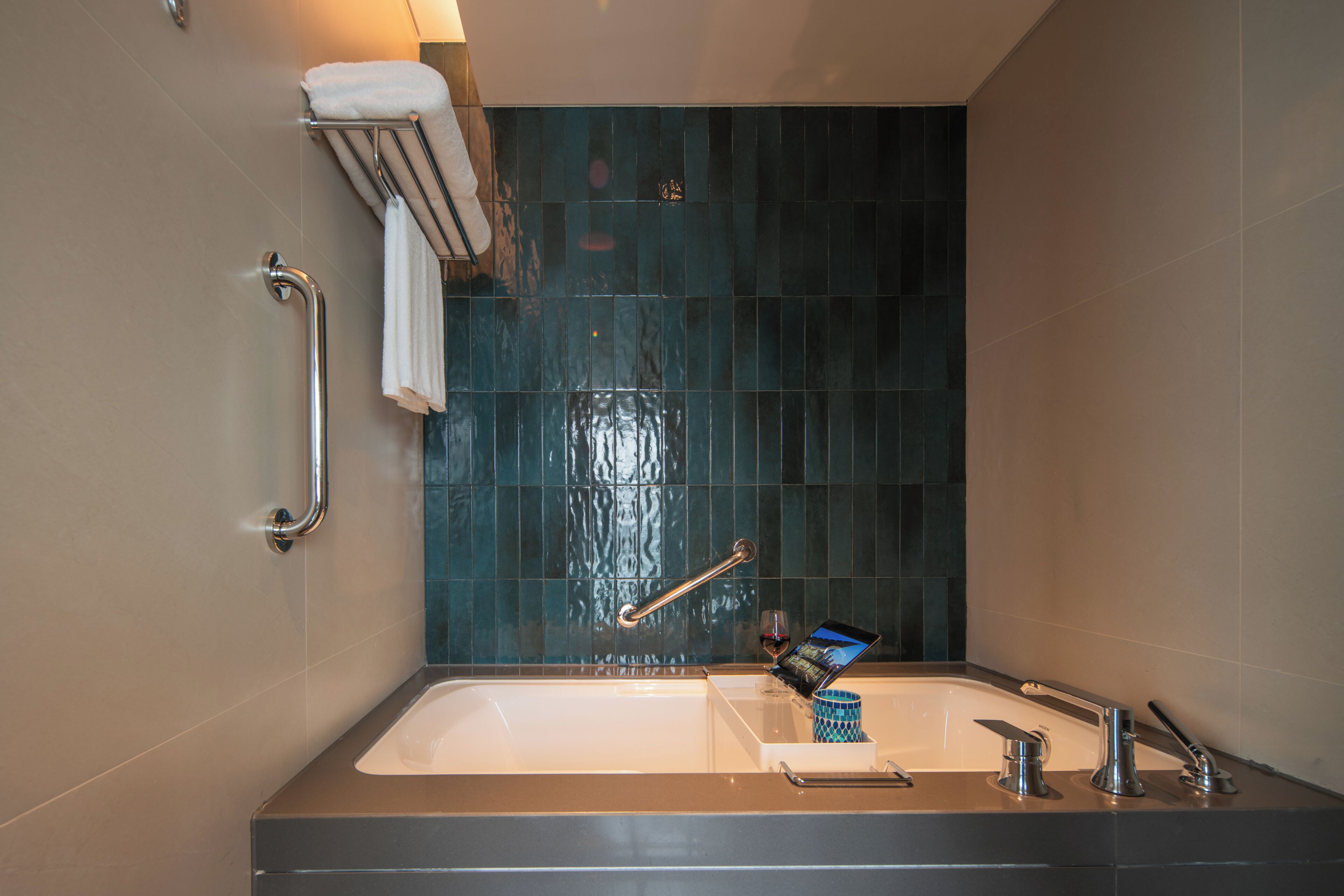 A modern bathroom with a bathtub, a handrail, a towel rack, and a glass of wine on the counter.