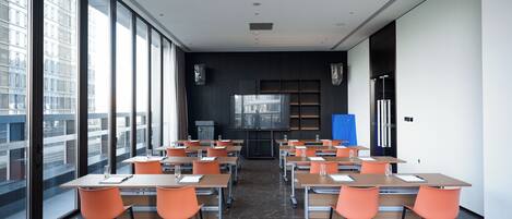 A modern conference room with large windows, a flat-screen TV, and orange chairs.
