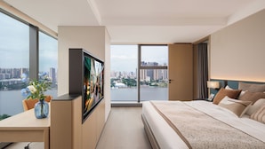 Habitación de hotel moderna con una cama grande, un escritorio con un florero, un televisor y vista a la ciudad.