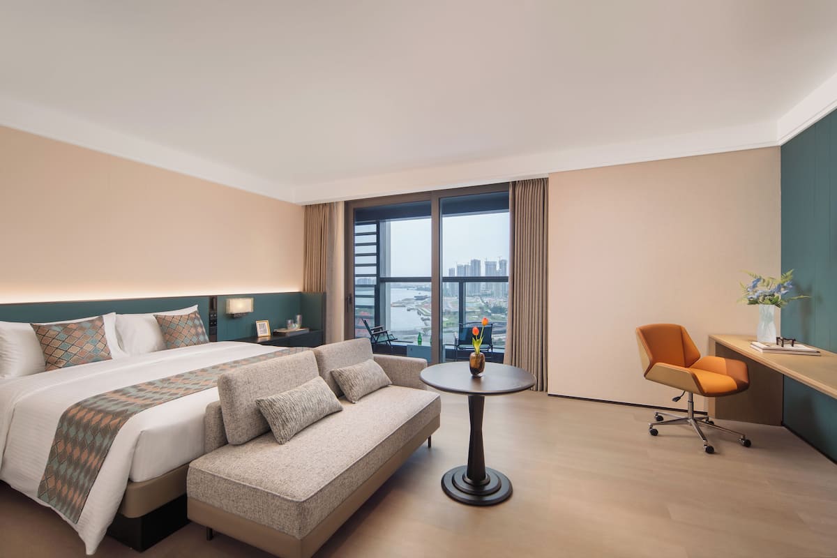 A hotel room with a bed, sofa, desk, and a view of the city.