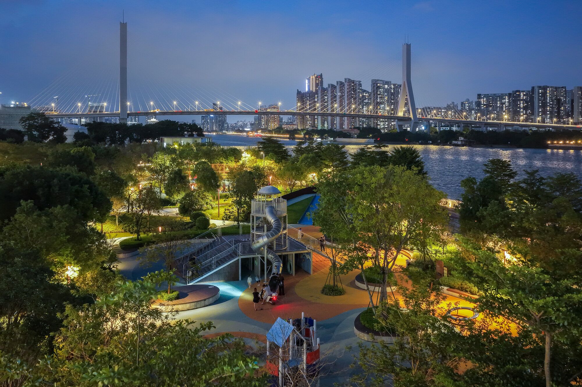 A park with playgrounds, a bridge, and a city skyline in the background.