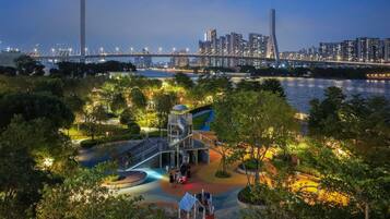 A park with playgrounds, a bridge, and a city skyline in the background.