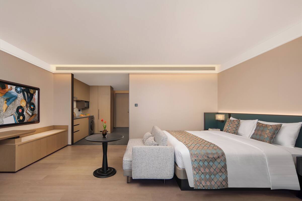 A hotel room with a bed, a seating area, a small table, and a painting on the wall.