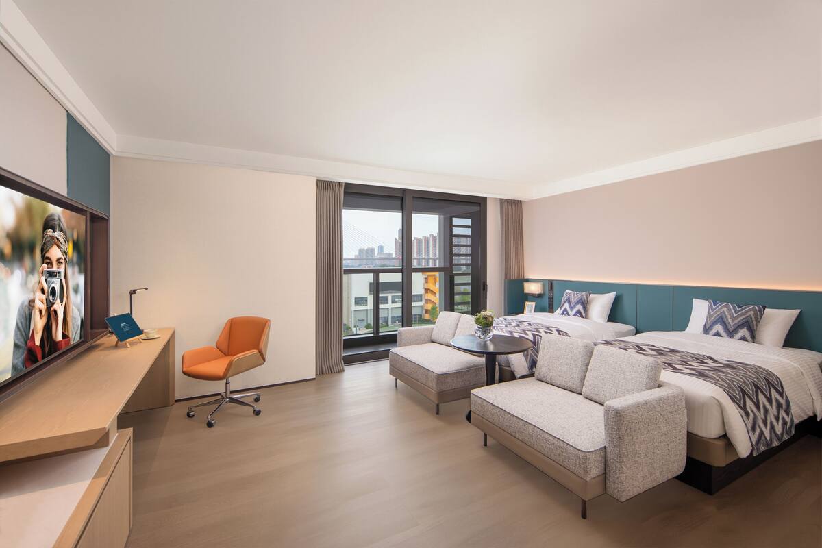 A hotel room with a bed, sofa, armchair, TV, and a city view.