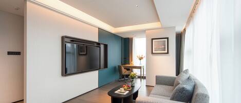 A modern living room with a flat-screen TV, a sofa, a coffee table with fruits, and a dining area with a table and chairs.