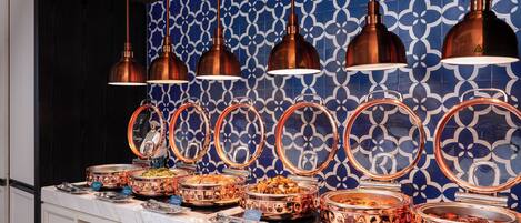 A buffet with multiple food stations, copper pendant lighting, and a patterned blue and white backsplash.