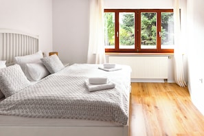 A bedroom with a bed, white bedding, a window with a view of greenery, and a wooden floor. - "Little Fox" vacation apartment - perfect for families with children and babies (Höchenschwand)