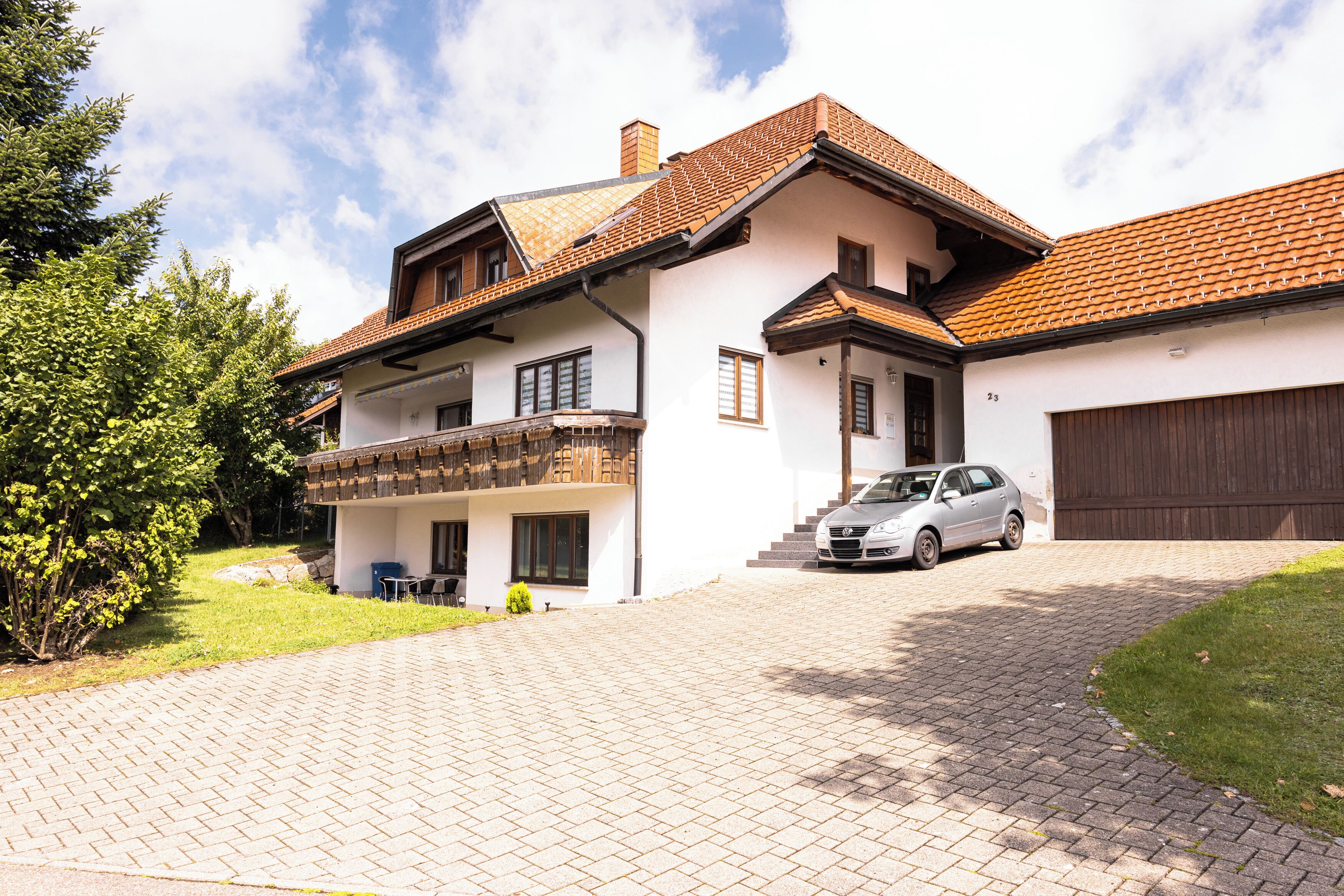 Een woonhuis met twee verdiepingen, een auto op de oprit, een balkon en een garage.