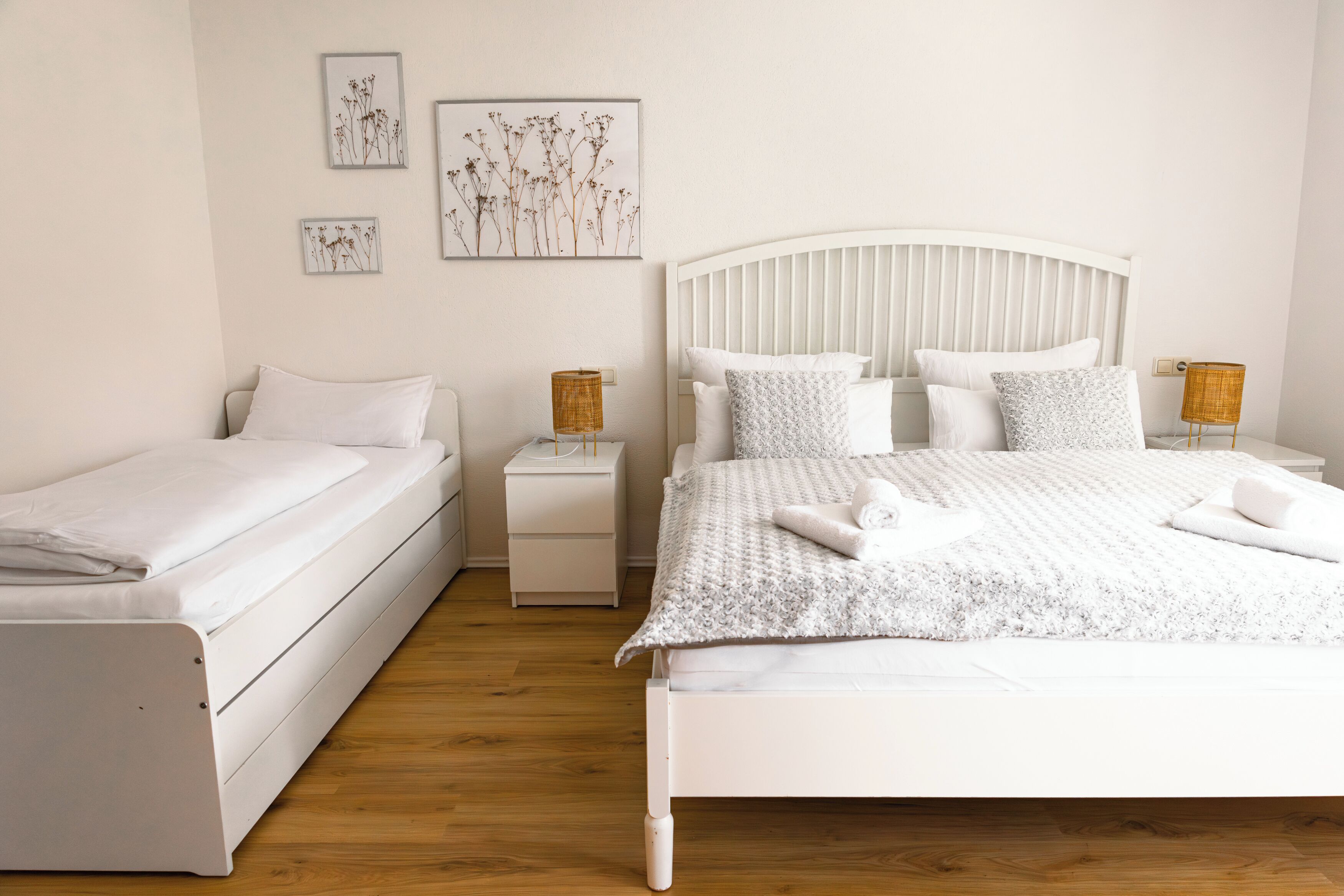 Un dormitorio con una cama individual, una cama más pequeña, dos mesitas de noche y una obra de arte colgada en la pared.