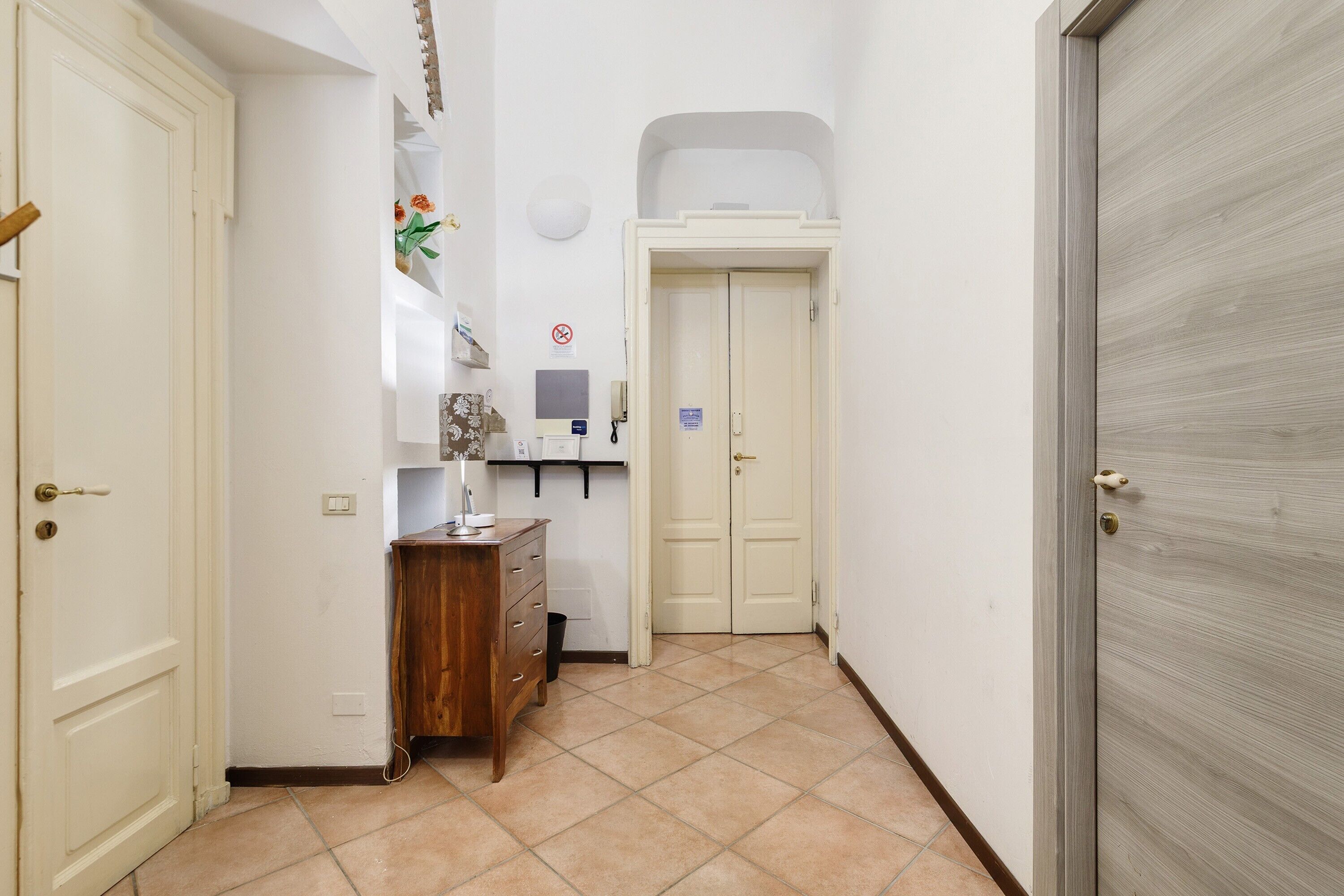 A hallway with a wooden dresser, a white door, and a tiled floor.