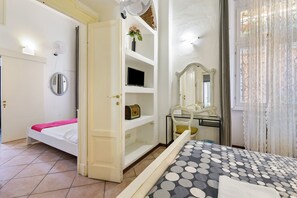 Ein Schlafzimmer mit einem Bett, einem Nachttisch, einem Spiegel, einem Regal mit einem Fernseher und einer Tür zu einem anderen Raum.