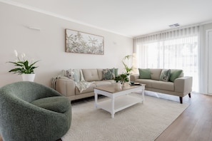 Een woonkamer met een bank, een salontafel, een groene fauteuil en een potplant.