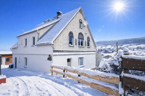 A white two-story house with a sloped roof, a wooden fence, and a clear blue sky.