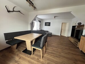 Ein modernes Wohnzimmer mit einem Holzesstisch, einer Sitzbank, einem grauen Sofa und einer Treppe, die zu einer oberen Ebene führt.