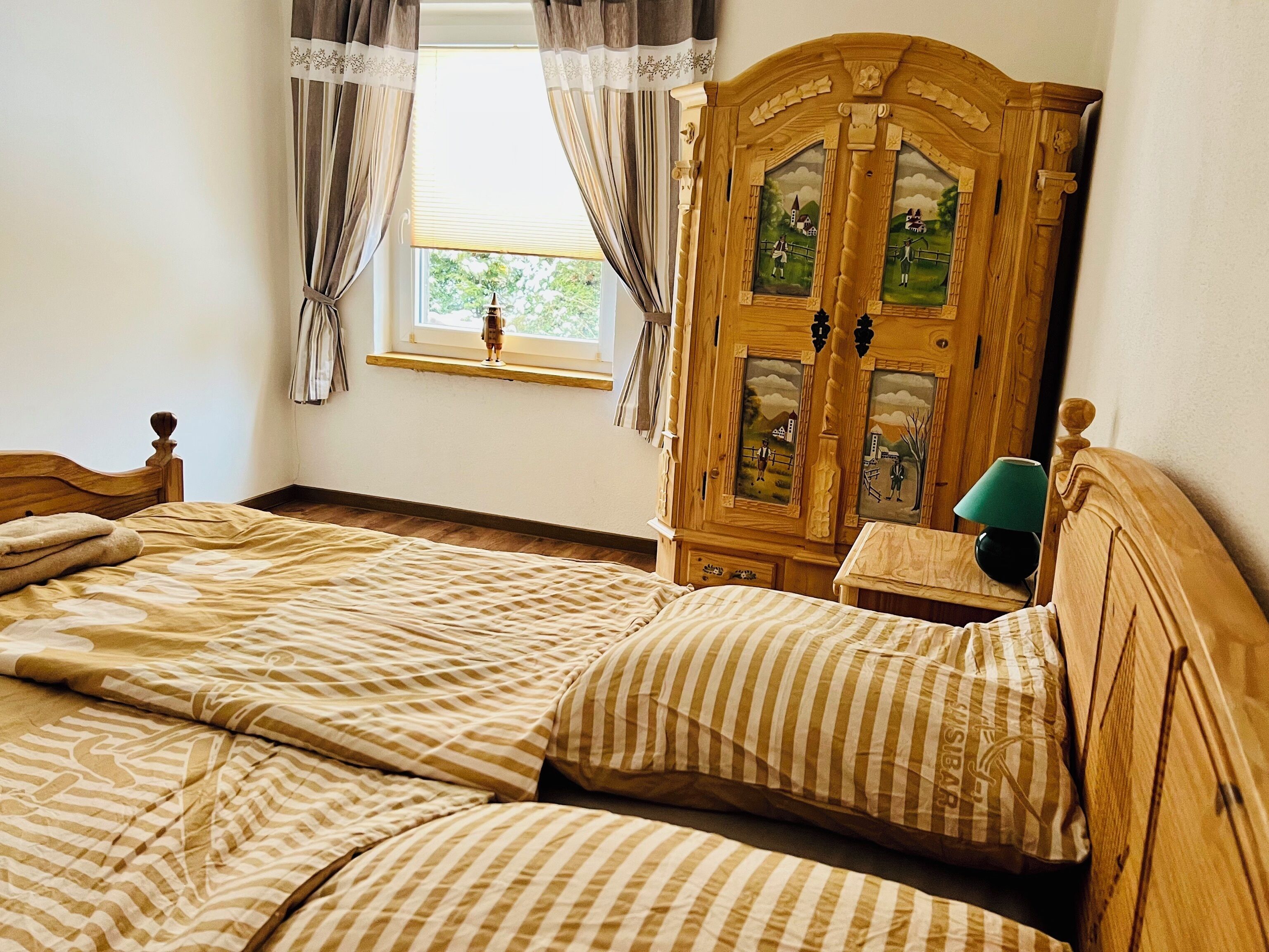 Un dormitorio con un armario de madera, una cama con ropa de cama a rayas y una ventana con cortinas.