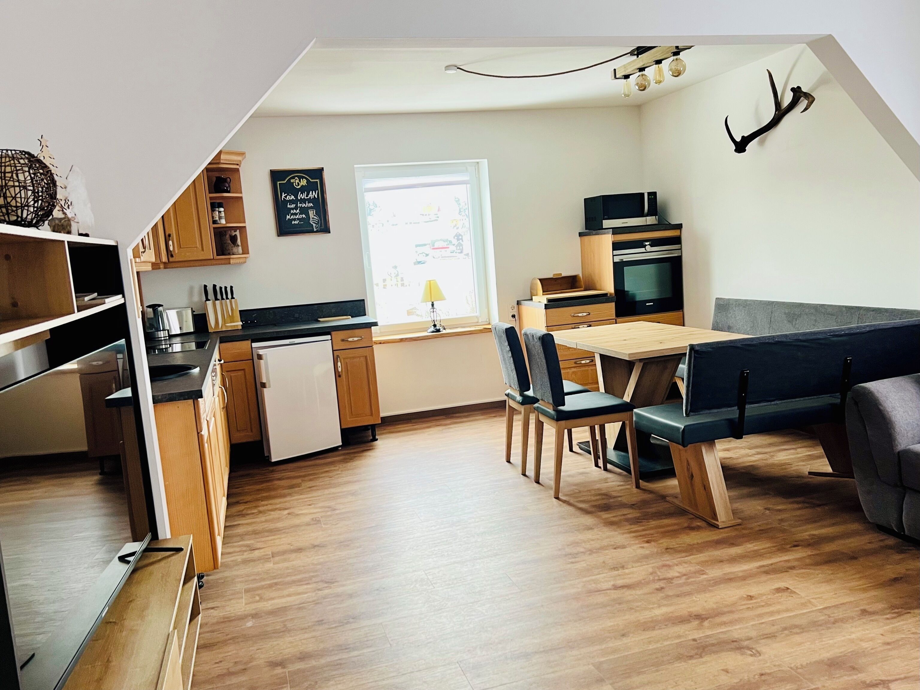 A modern kitchen with wooden cabinets, a built-in oven, and a dining area with a bench and chairs.