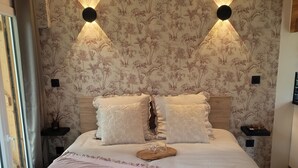 Quarto com uma cama grande, papel de parede floral, duas luminárias fixadas na parede e uma cabeceira de madeira.