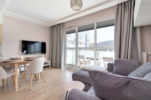 Un salon moderne comprenant un canapé, une table à manger avec des chaises, un téléviseur à écran plat et une grande fenêtre avec des rideaux.
