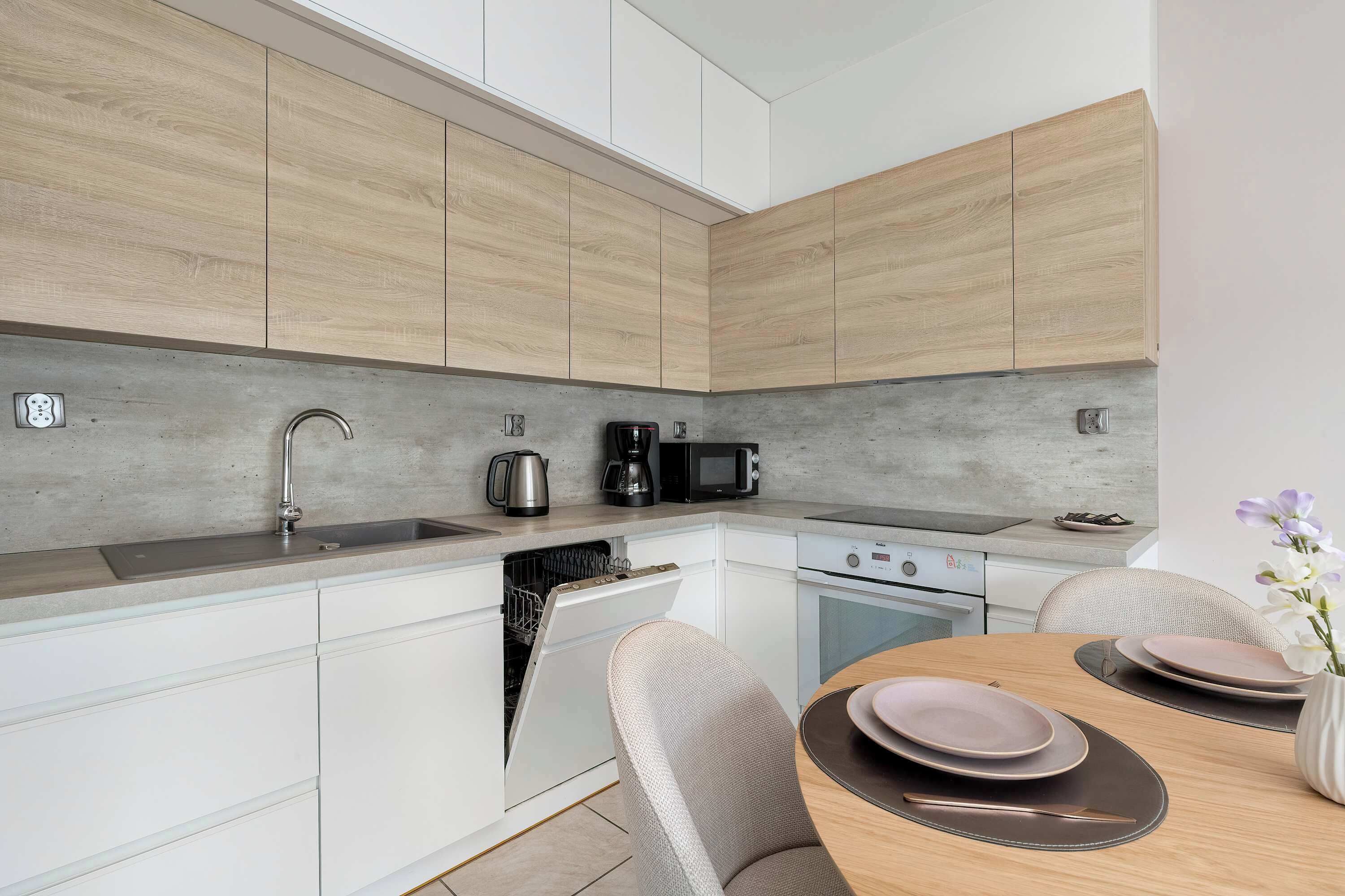 A modern kitchen with wooden cabinets, a dishwasher, a microwave, and a dining area with a table set for two.